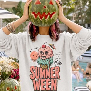 May include: A white long-sleeve sweatshirt featuring a graphic of a melting ice cream cone with a skull face, a cherry, and a small umbrella. The text reads "SUMMER WEEN" and "I scream You scream We all scream for" with a sunset, bats, and palm trees.