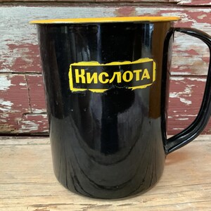 May include: Black enamel pitcher with a yellow rim and handle. The pitcher has the word "KISLOTA" written in yellow letters on the front.