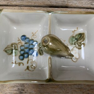 May include: A white ceramic divided serving dish with a green and blue grape design and a green pear-shaped accent.