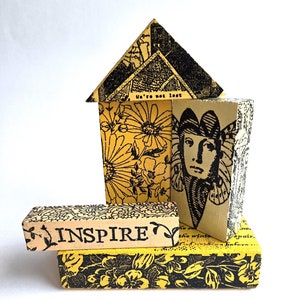 May include: A yellow and black wooden house-shaped sculpture with the words "We're not lost" and "INSPIRE" on it. The sculpture is decorated with floral and butterfly patterns.