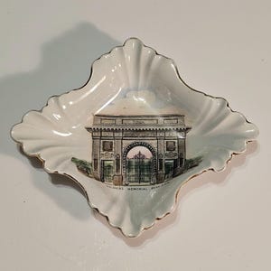 May include: A white ceramic dish with a gold rim and a depiction of the Soldiers' Memorial Arch in Boston, Massachusetts. The dish is shaped like a diamond and has a scalloped edge.