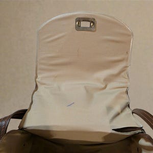 Puede incluir: Vista abierta de un bolso de mano de cuero marr&oacute;n con interior beige. La solapa del bolso est&aacute; abierta, revelando un forro de tela beige y un cierre met&aacute;lico. Las asas del bolso son visibles a ambos lados.
