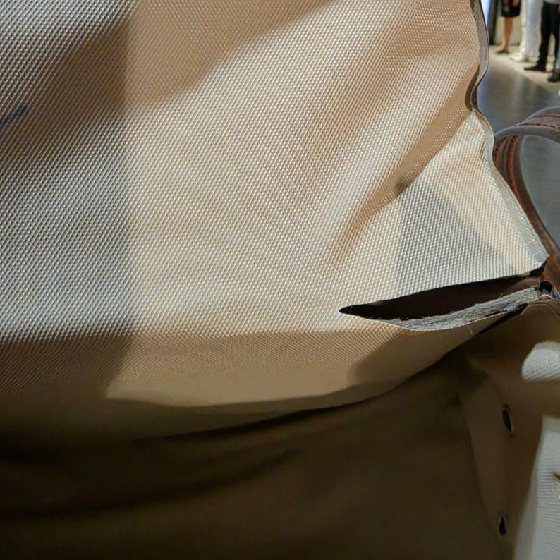 Puede incluir: Bolso de tela color beige con asa de cuero marr&oacute;n. El bolso tiene un desgarro en la tela, revelando el interior. El bolso parece estar vac&iacute;o.