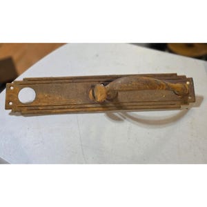 May include: An antique bronze door handle with a rectangular backplate and a curved handle. The handle has a weathered, aged appearance, with visible signs of wear and tear. The backplate features a circular hole and two smaller holes for mounting.
