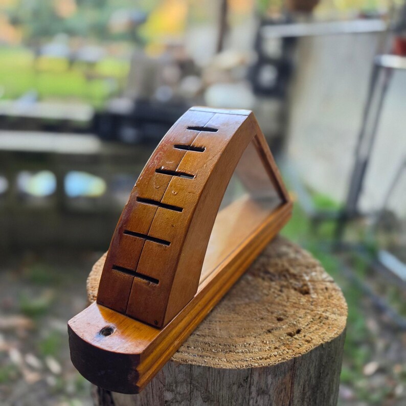 May include: A wooden knife block with a curved top and several slots for knives. The block has a clear glass front and is made of a warm-toned wood. It is displayed on a tree stump.