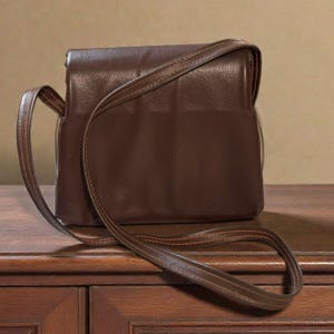 Puede incluir: Un bolso bandolera de cuero marr&oacute;n con cierre de solapa y una correa larga y ajustable. El bolso es rectangular con esquinas redondeadas y un ribete cosido. La correa tambi&eacute;n es marr&oacute;n y parece del mismo material que el bolso.