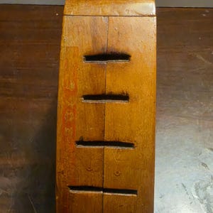 May include: A vertical, wooden box with a warm, brown finish. The box has four horizontal slots cut into the front. The wood grain is visible, and the box appears to be aged. The box is likely a vintage item.