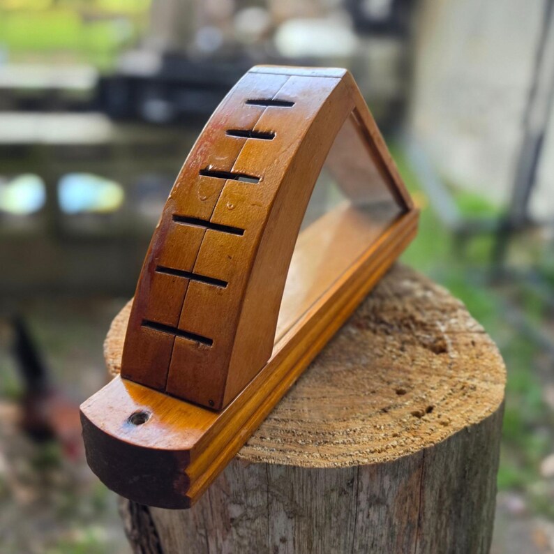 May include: A wooden knife block with a curved top and a clear glass display area. The block has several slots for knives and is made of a warm-toned wood. The knife block is sitting on a tree stump.