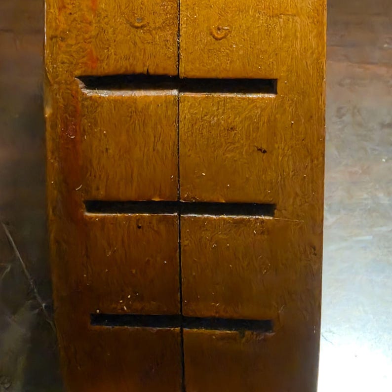 May include: Close-up of a rectangular, wooden object with a warm, brown hue. The wood grain is visible, and there are three horizontal, rectangular cutouts. The object appears to be a component of a larger structure or piece of furniture.