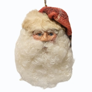 May include: A Santa Claus face ornament with a red and brown patterned hat, a cream-colored fluffy beard, and a painted face. The ornament has a gold string for hanging and is set against a white background.
