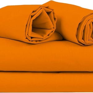Può includere: Un set di lenzuola arancioni brillanti, tra cui un lenzuolo piano, un lenzuolo con angoli e due federe arrotolate. Le lenzuola sono ben piegate e impilate, mostrando un colore solido e vibrante. Il set di biancheria da letto è realizzato in materiale liscio.