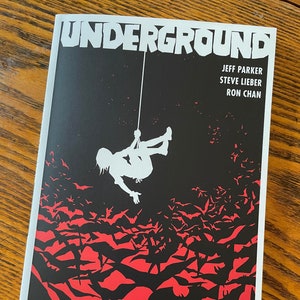 May include: A comic book cover with the title "UNDERGROUND" in bold white letters. The cover features a silhouette of a person hanging from a rope against a black background with a red and black pattern of bats.