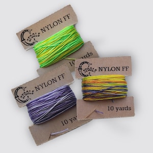 May include: Several spools of nylon thread in various colors, including green, yellow, purple, and orange. Each spool is labeled with "SPOOLS NYLON FF" and "10 yards" on a brown tag. The spools are arranged on a light background.