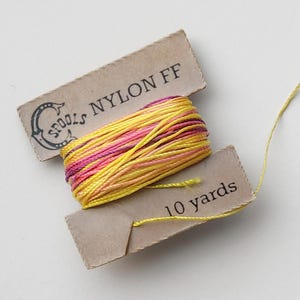 May include: A spool of nylon thread in shades of yellow and pink, with a brown label that reads "NYLON FF" and "10 yards". The spool is labeled "SPOOLS".