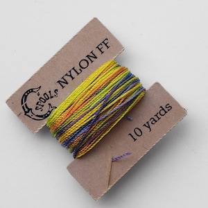 May include: A spool of multi-colored nylon thread, with yellow, orange, and purple hues. The thread is wrapped around a cardboard card that reads "SPOOLS NYLON FF" and "10 yards". The spool is ideal for crafting and sewing projects.