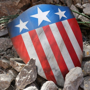 May include: A red, white, and blue shield with a distressed look. The shield has five white stripes and four red stripes. There are three white stars on the blue field.