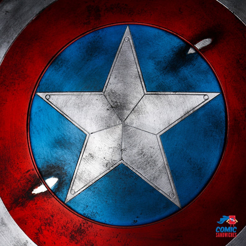 Puede incluir: Un escudo de bandera americana rojo, blanco y azul con una gran estrella plateada de cinco puntas en el centro. El escudo est&aacute; desgastado y deteriorado, con ara&ntilde;azos y rozaduras visibles.