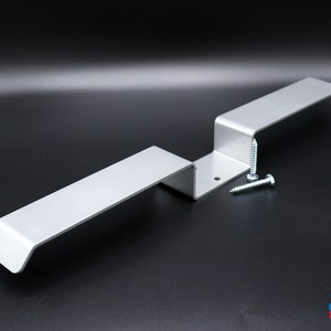 May include: A silver metal bracket with two arms and two screws. The bracket is designed to be attached to a wall or other surface.