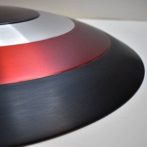May include: A close-up of a red, white, and black Captain America shield. The shield is made of metal and has a shiny finish.