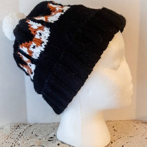 May include: Black knit beanie with a white pom pom and a brown and white knit pattern on the brim.