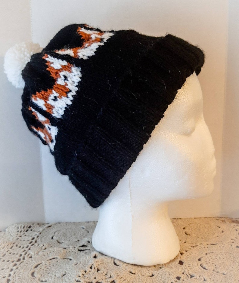 May include: Black knit beanie with a white pom pom and a brown and white knit pattern on the brim.