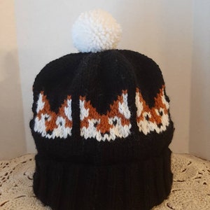 May include: Black knit beanie with a white pom pom and a pattern of three orange foxes on the front.