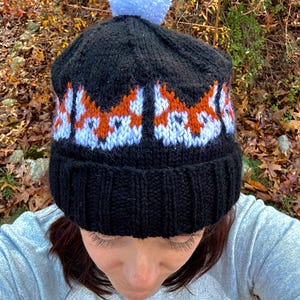 May include: Black knit beanie with a white pom pom and a repeating pattern of orange and white fox faces.