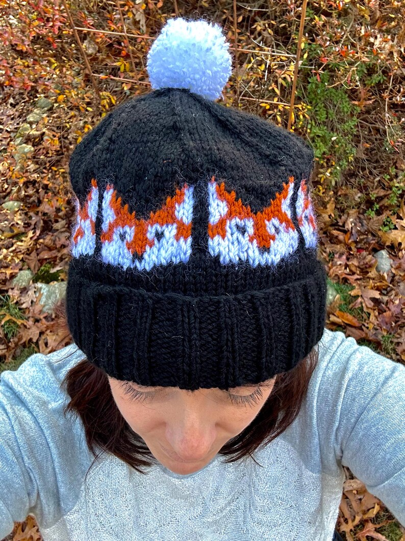 May include: Black knit beanie with a white pom pom and a repeating pattern of orange and white fox faces.