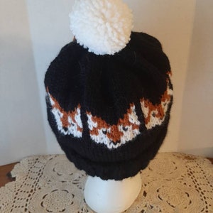 May include: Black knit beanie with a white pom pom and a pattern of orange fox faces.