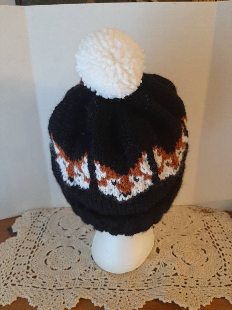 May include: Black knit beanie with a white pom pom and a pattern of orange fox faces.