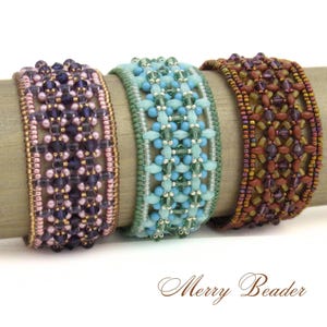 Pode incluir: Três pulseiras de punho com contas nas cores roxo, turquesa e marrom. As pulseiras são feitas com pequenas contas e cristais e são exibidas em um pino de madeira. O texto "Merry Beader" está na parte inferior.