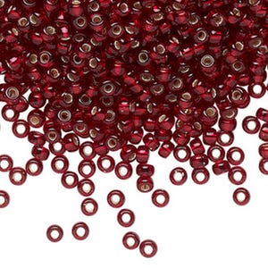 May include: A large pile of small, round, red glass beads with a silver coating. The beads are scattered on a white background.