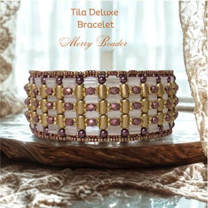 May include: A beaded bracelet with the text "Tila Deluxe Bracelet" and "Merry Beader". The bracelet features a pattern of gold, purple, and clear beads. The bracelet is approximately 3.8 cm wide.