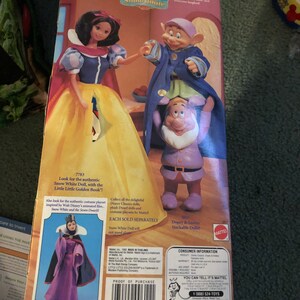 Puede incluir: Una caja para un juego de mu&ntilde;ecas de Blancanieves con una imagen de Blancanieves y Dopey. La caja es amarilla y presenta una imagen de Blancanieves y Dopey. La caja tambi&eacute;n incluye una imagen de la Reina Malvada. La caja est&aacute; etiquetada como "Disney Classics" y "Blancanieves".