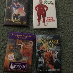 May include: Four VHS tapes featuring Disney movies. Titles include "A Kid in King Arthur's Court", "The Santa Clause", "The Aristocats", and "Homeward Bound II: Lost in San Francisco". Each tape has colorful artwork and text.