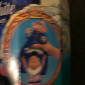 Puede incluir: Primer plano de un conjunto de juguetes vintage de Blancanieves y los Siete Enanitos. El conjunto incluye dos enanos, uno con un atuendo azul y el otro con un atuendo morado. Los enanos se toman de la mano y sonr&iacute;en. El conjunto est&aacute; enmarcado en un &oacute;valo dorado.