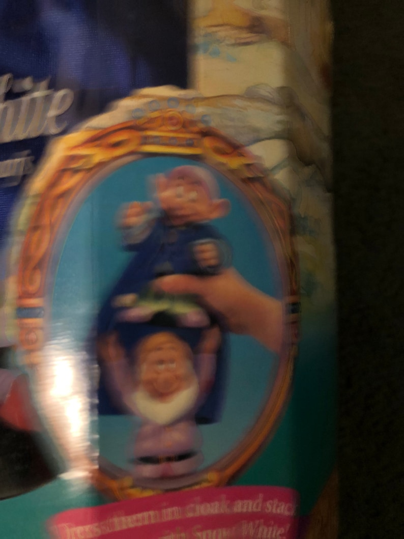 Puede incluir: Primer plano de un conjunto de juguetes vintage de Blancanieves y los Siete Enanitos. El conjunto incluye dos enanos, uno con un atuendo azul y el otro con un atuendo morado. Los enanos se toman de la mano y sonr&iacute;en. El conjunto est&aacute; enmarcado en un &oacute;valo dorado.