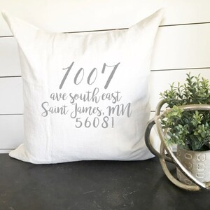 May include: White throw pillow with gray text that reads "1007 ave southeast Saint James, MN 56081".