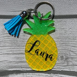 May include: A yellow and green glitter pineapple keychain with a blue tassel and the name "Laura" written on it.
