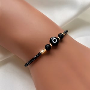 May include: Black beaded bracelet with three gold beads and a blue evil eye charm.