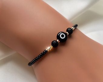 May include: Black beaded bracelet with three gold beads and a blue evil eye charm.