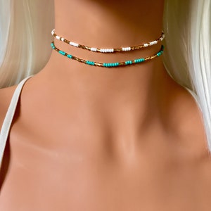 May include: A layered choker necklace with turquoise, white, and gold beads.