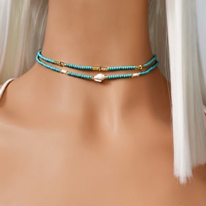 May include: A turquoise and gold beaded choker necklace with a white shell charm.