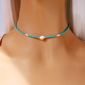 May include: A turquoise and gold beaded choker necklace with a white shell charm.