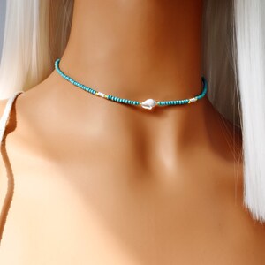 May include: A turquoise and gold beaded choker necklace with a white seashell charm.
