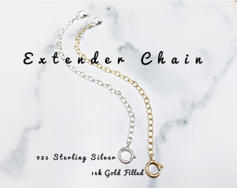 May include: Two extender chains, one silver and one gold, on a white marble background. The text "Extender Chain" is written above the chains. The text "925 Sterling Silver" is written below the silver chain and the text "14k Gold Filled" is written below the gold chain.