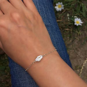 May include: A delicate gold chain bracelet with a white seashell charm. The bracelet is worn on a person's wrist.