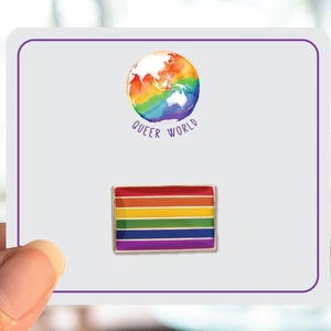 May include: A white card with a rainbow globe and the text "Queer World". Below the globe is a rainbow enamel pin in the shape of a flag.