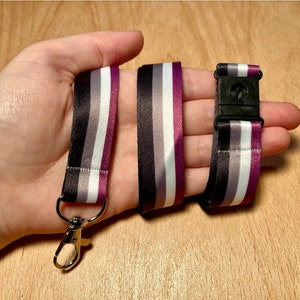 May include: A black, white, gray, and purple striped lanyard with a silver swivel clip and a black plastic buckle.