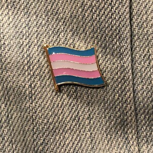 May include: A blue, pink, and white transgender pride flag pin on a denim background.